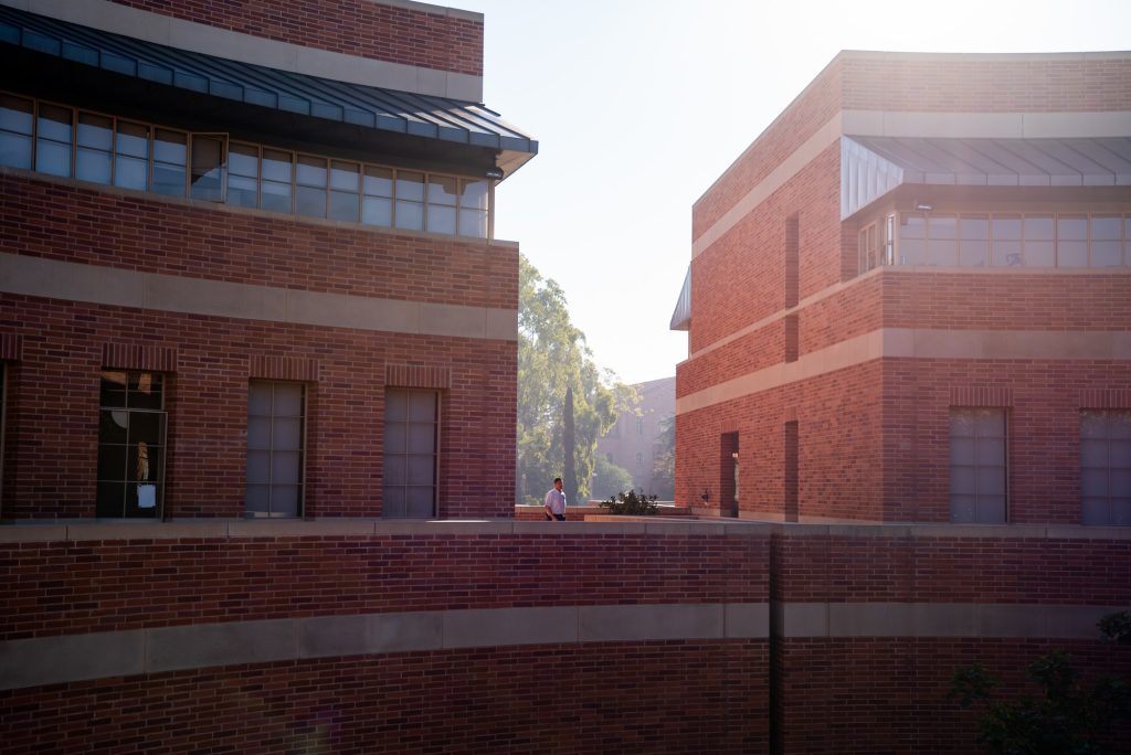 A worker walks between Entrepreneurs Hall and Cornell Hall in the morning light. The circular terrace weaves between the two buildings and continues to the right, eventually connecting with Gold Hall to the west. Photographed by Julia Gu/BruinLife.