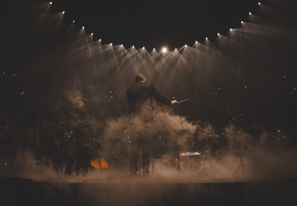 A conductor, back turned to the camera, guides an orchestra. Prior to taking the stage, Bad Bunny had a full orchestra perform on the arena's B-stage, providing an immersive melodic array that set the scene for the night ahead.