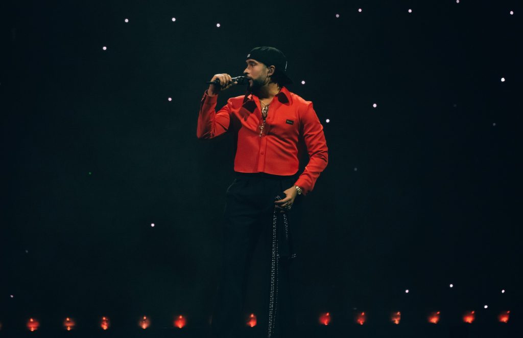 Bad Bunny faces left as he sings into the mic onstage. Taking the stage by storm, Bad Bunny exuded pure confidence and vivacity throughout his performance, ensuring all in attendance would have a night to remember.