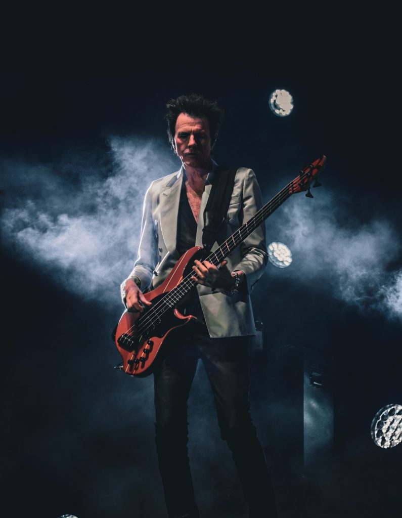 Bass guitarist John Taylor of Duran Duran sports a dapper light blazer as he plays on an eclectic red bass. Photographed by Cathryn Kuczynski/BruinLife