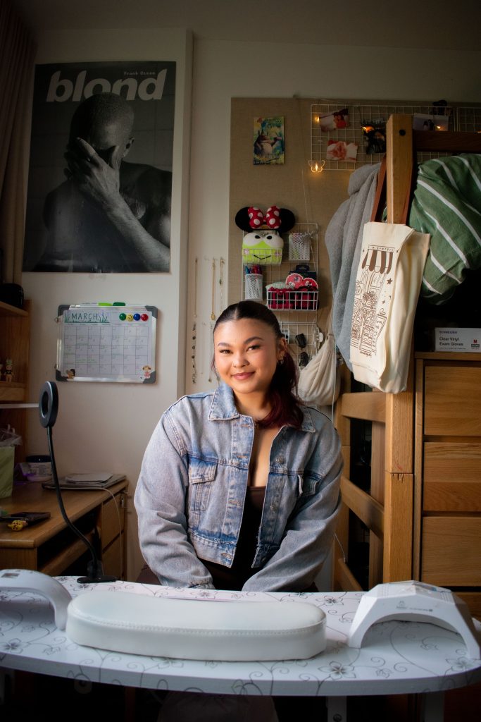 Mia Pryzbus smiles in her dorm in front of her nail station. This is the workspace she has created to do fellow UCLA students' nails. Photographed by Emily Chandler/BruinLife