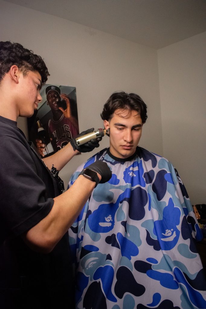 Diego Duarte cleans up a client's cut with a razor in the room where he runs his barbering business. Photographed by Emily Chandler/BruinLife