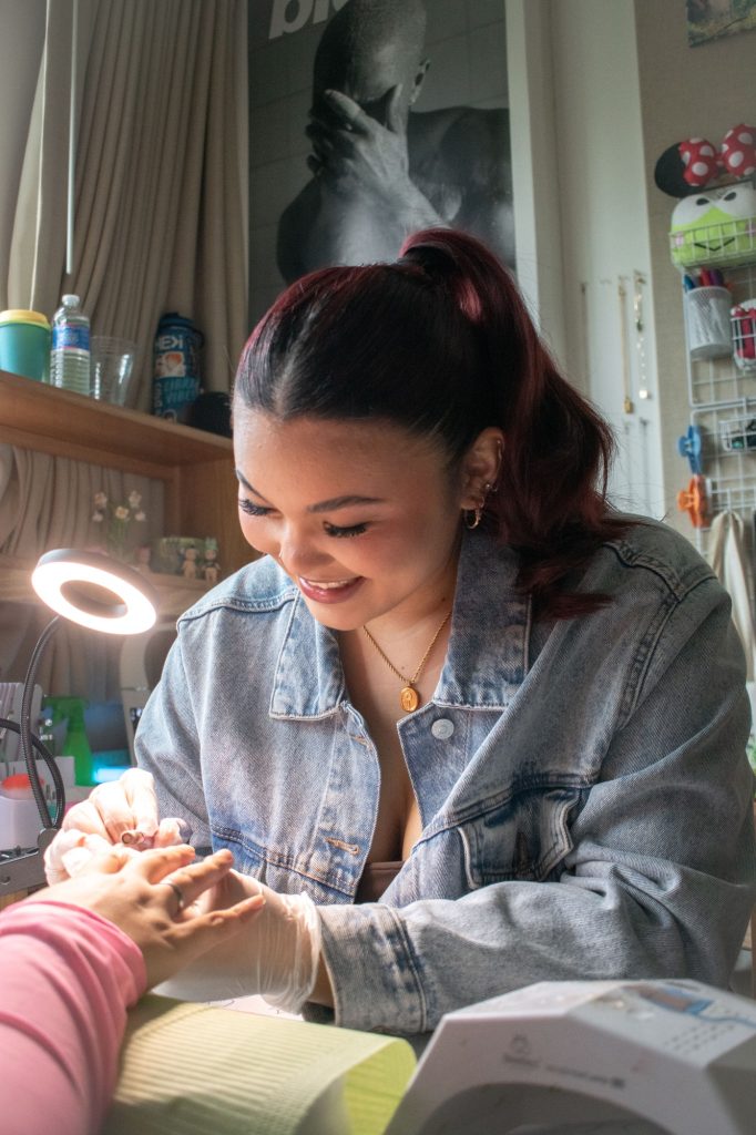 Mia Pryzbus smiles as she works on a client's nail set. Pryzbus has created a workspace in her dorm room. Photographed by Emily Chandler/BruinLife