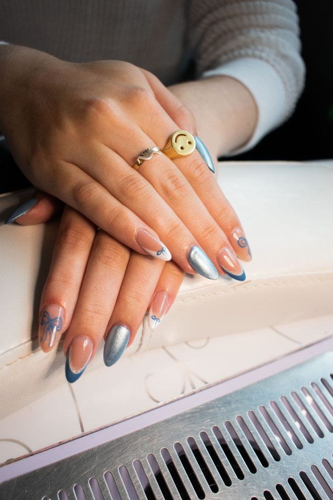 Client shows off her nail set done by Mia Pryzbus: a blue and chrome based “coquette” themed set. Photographed by Emily/BruinLife