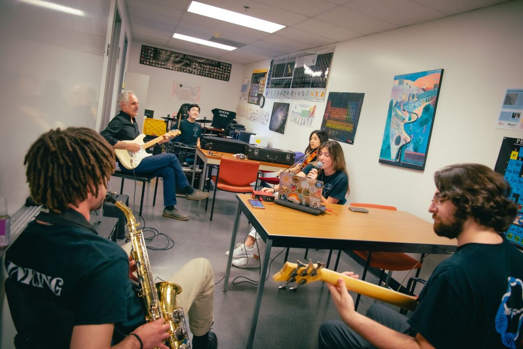 The Sinking Ducks perform in an office lobby space on the fourth floor of W.G. Young Hall, amidst walls covered with science infographics. Photographed by BruinLife/Finn Martin