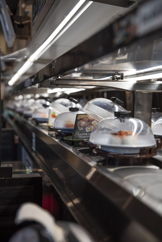 Dishes pass by on the conveyor belt. Photographed by Emily Chandler/BruinLife.