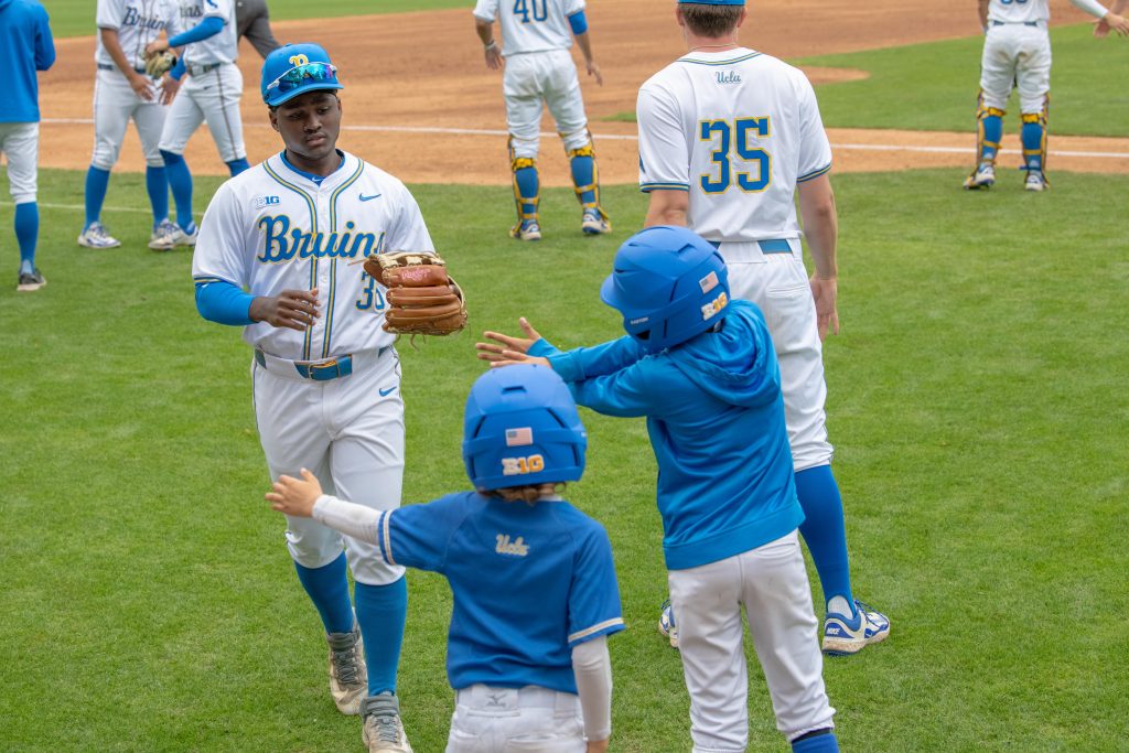 Outfielder #36, Dean West, shares a moment with young fans on the field with high-fives. Photographed by Maia Salti/BruinLife