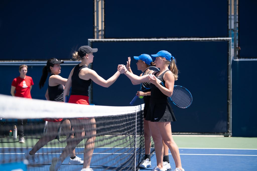 Rutgers and UCLA players greet each other with high fives after finishing a doubles match.
