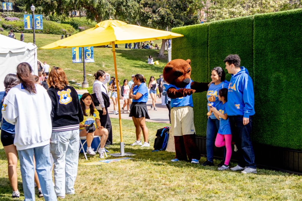 As the photographer prepares for a photo shoot, Joe Bruin entertains the young sister of an admitted student, bringing out authentic smiles and laughs from the family in Wilson Plaza. Photographed by Julia Gu/BruinLife.