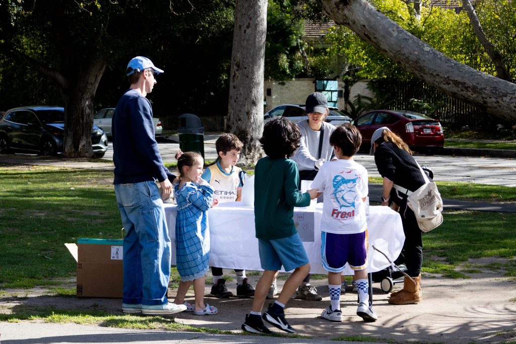 A forward-planning young boy (third from the left) runs a lemonade and cookie stand to – as per his father (left) – save up for Legos and college. Photographed by Julia Gu/BruinLife.