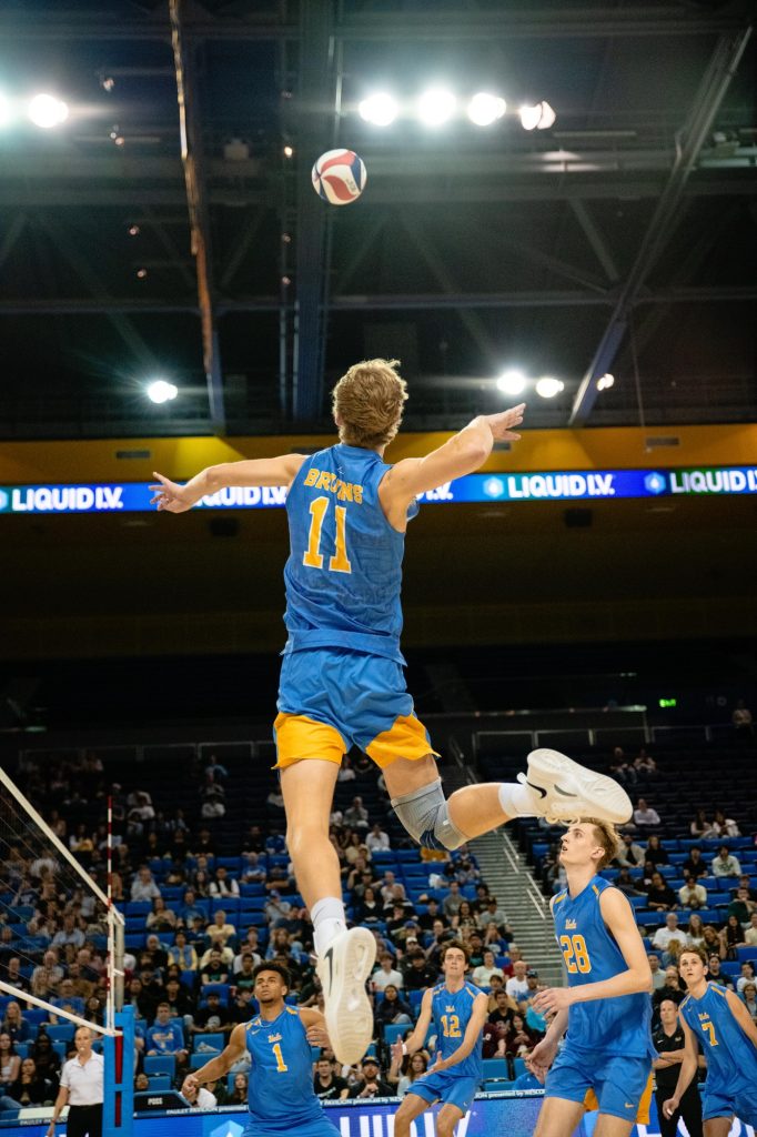 UCLA's Cooper Robinson leaps high to spike the ball over BYU blockers. Photographed by Ryan Zhang/BruinLife.