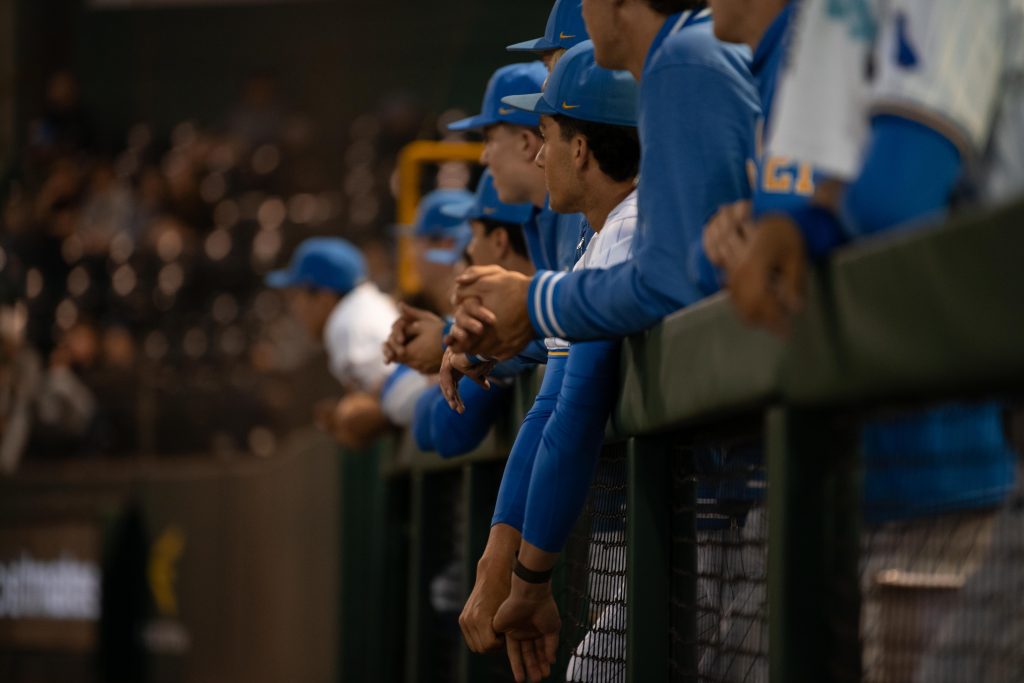 UCLA players lean over dug out railing as they watch their teammates at bat.