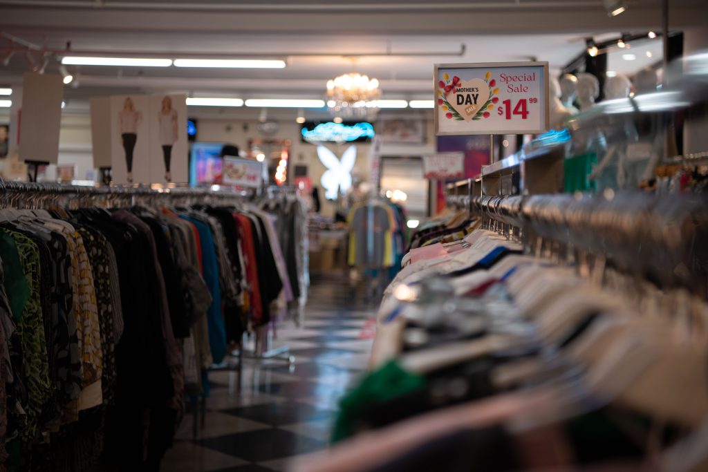 Aisle of clothes ranging from all sizes with playboy bunny sign in background.