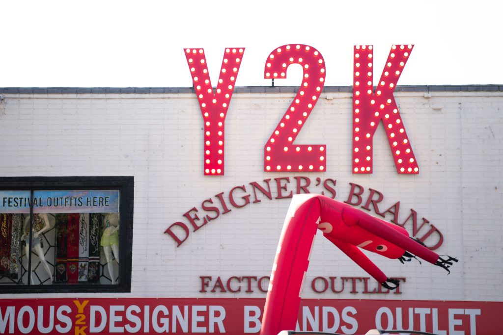 Store's Y2K Designers Brand sign outside front of building behind stores inflatable red tube man.
