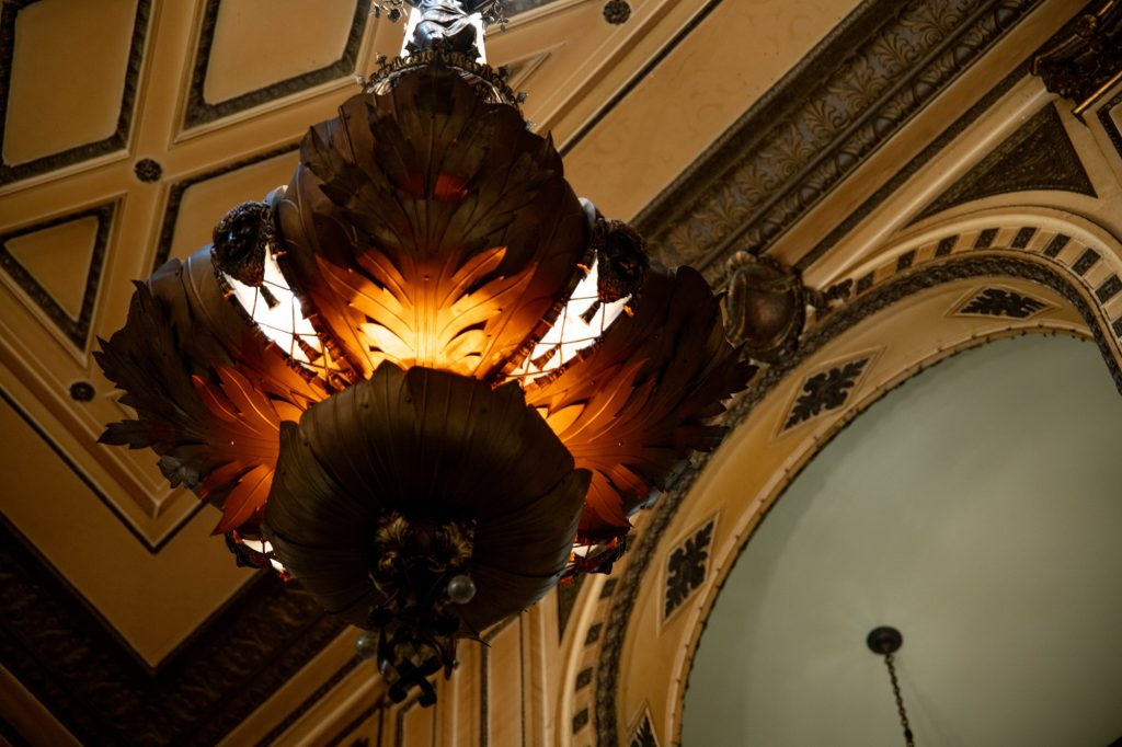 A beautiful light fixture hangs from the ceiling of the Orpheum Theatre and illuminates the space with a warm glow. Photographed by Julia Gu/BruinLife.