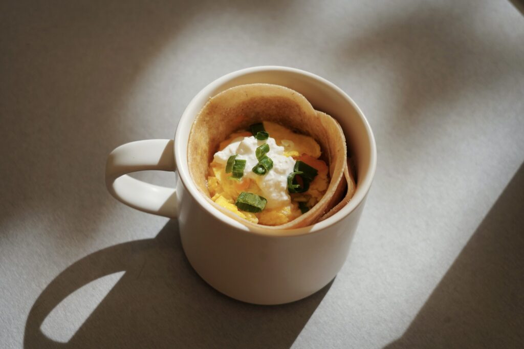A burrito in a mug stuffed with fluffy eggs and melted cheddar, topped with sour cream and scallions. Photographed by Polly Lee/BruinLife.
