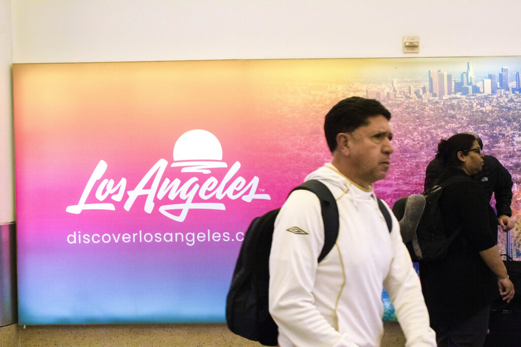 A lone man passes by a sign advertising the city of angels as he rushes across the American Airlines terminal. In the aftermath of the government shutdown, passengers were stranded in America's worst airport — forced to wander the hallowed terminals of LAX like hungry ghosts. Photographed by Gavin Meichelbock/BruinLife.