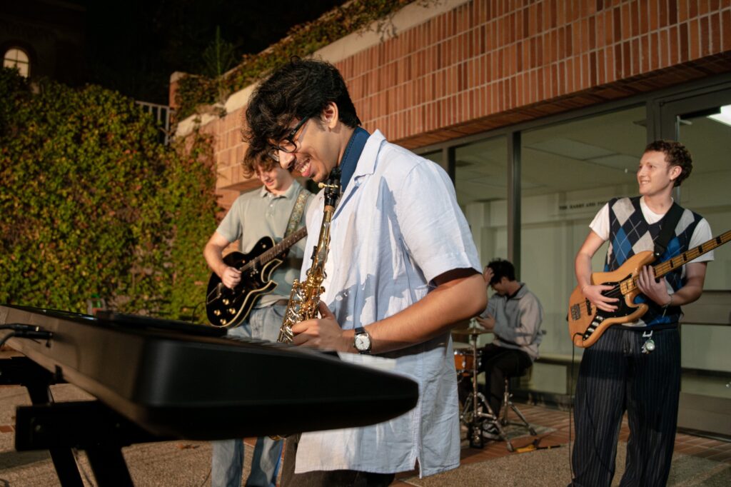 9 Ball, a UCLA-based indie rock band, pictured smiling as they perform at the ongoing concert series, Fowler Out Loud. Jai Raman, the keyboard and saxophone player, was absorbed in the moment as he performed a solo alongisde his band. Photographed by Siena Hunt/BruinLife