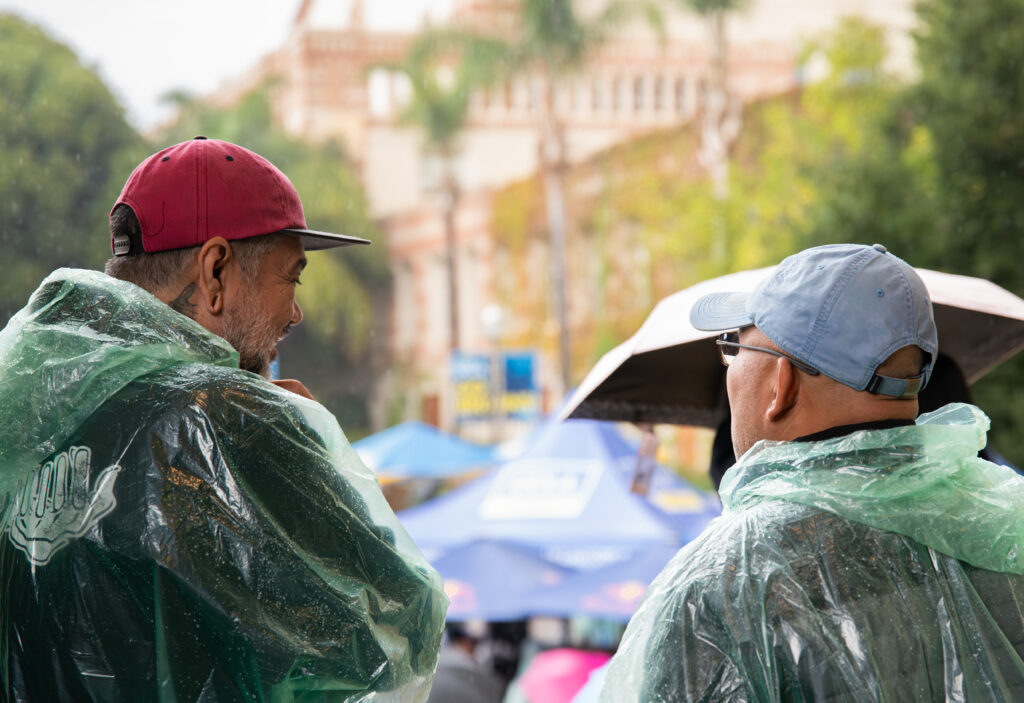 Two colleagues share a smile as they watch the strike from a sheltered spot out of the rain. Their lively conversation contrasted with the rainy scene beyond. Photographed by Siena Hunt/BruinLife