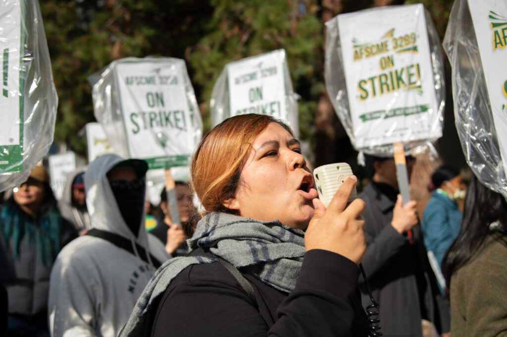 A volunteer pictured using a megaphone and chanting with the crowd. Moments earlier, those participating in the strike had just walked around Westwood cheering and vocalizing their frustrations. Photographed by Siena Hunt/BruinLife