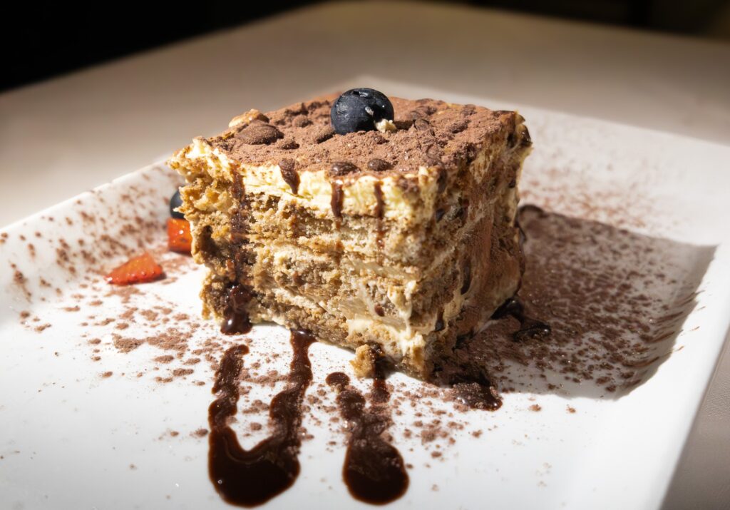 A slice of tiramisu sits beautifully plated on the table, lightly dusted with cocoa. The mascarpone and espresso flavors blended into a sweet and satisfying coffee-rich bite. Photographed by Siena Hunt/BruinLife