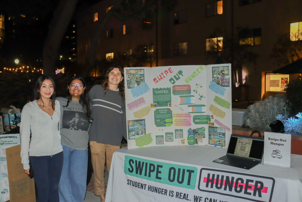 Three students man the Swipe Out Hunger booth at Sustainival. Swipe Out Hunger has collected and donated students' extra swipes at the end of the quarter, donating them to people who struggle with food insecurity. Photographed by Regan Rhodes/BruinLife.