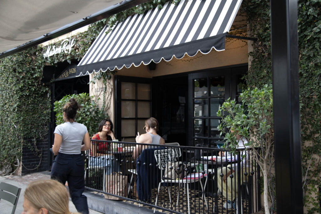 The people are chatting while enjoying the greenery and coffee on the balcony outside of Alfred Cafe on Melrose Place. Photographed by Aaron Fu/BruinLife.