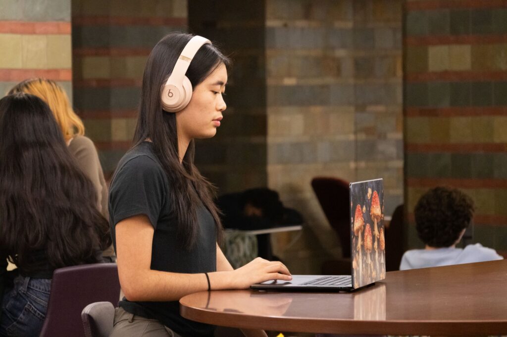 Second-year student Eunnie Wu tunes in to the Bruin Success Podcast on a quiet, rainy evening inside Powell Library. Photographed by Jaclyn Wang/BruinLife.