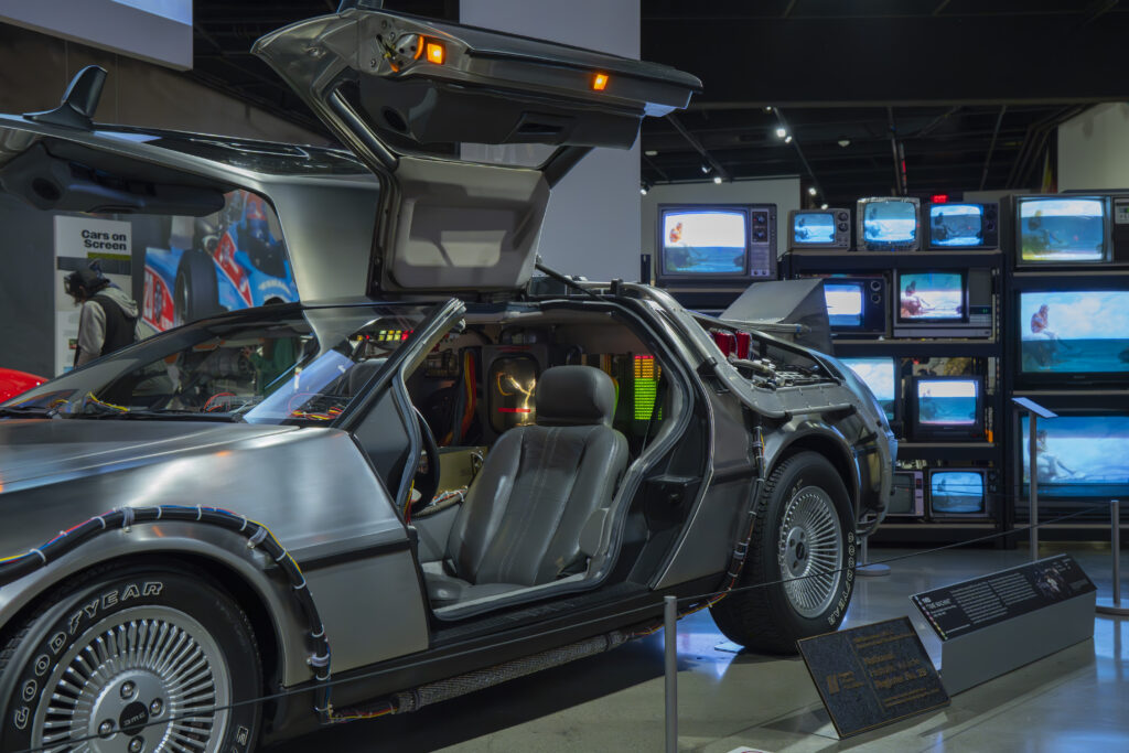 The DeLorean sits with doors raised, surrounded by vintage screens and sci-fi nostalgia. It channels cinematic time-travel magic. Photographed by Janwayne Orme/BruinLife.